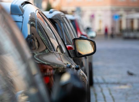 rows of different cars parked along the roadside in crowded city